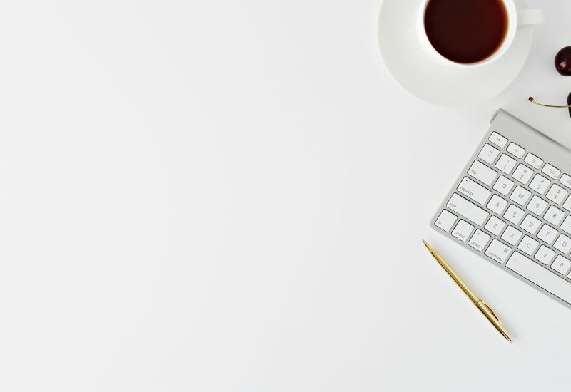 Keyboard, notebook and coffee on a white desk