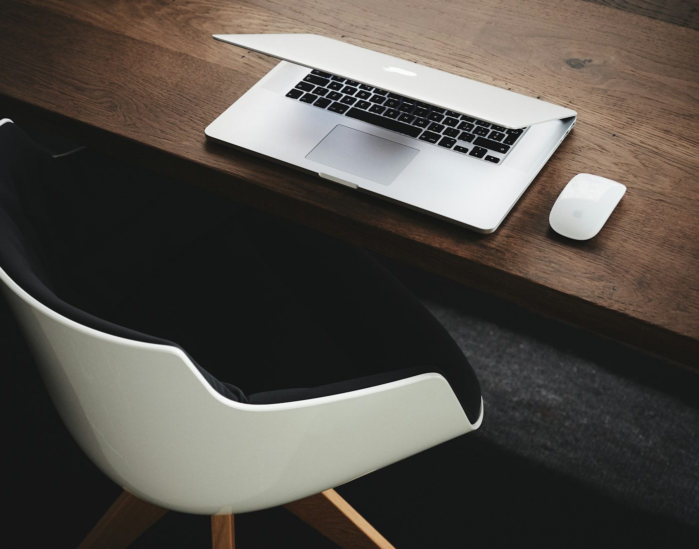 Laptop and mouse on a dark desk beside a chair