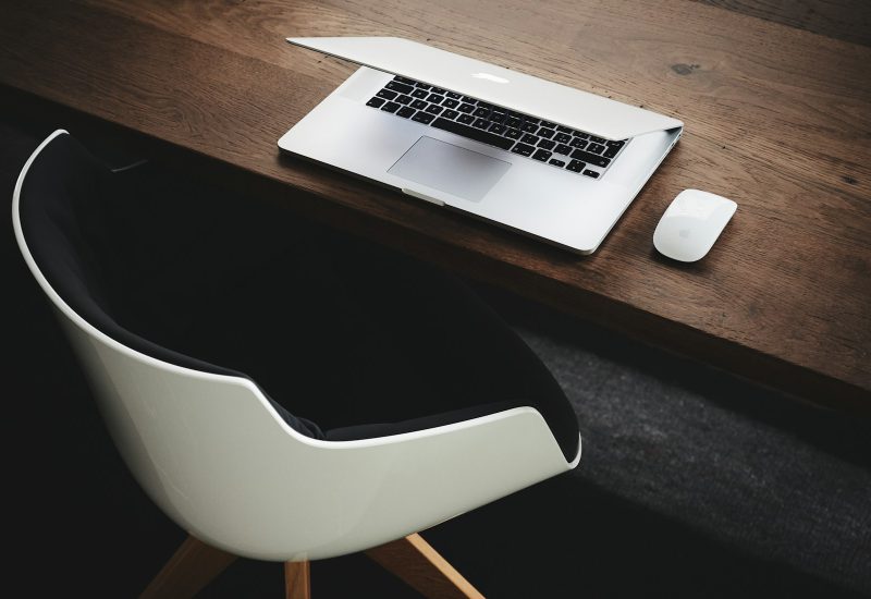 Laptop and mouse on a dark desk beside a chair