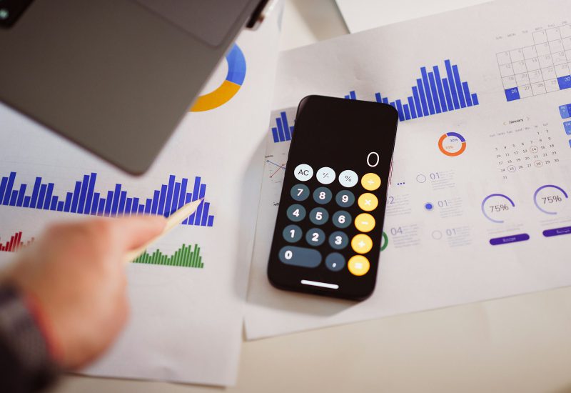 Calculator app on a phone beside printed financial charts