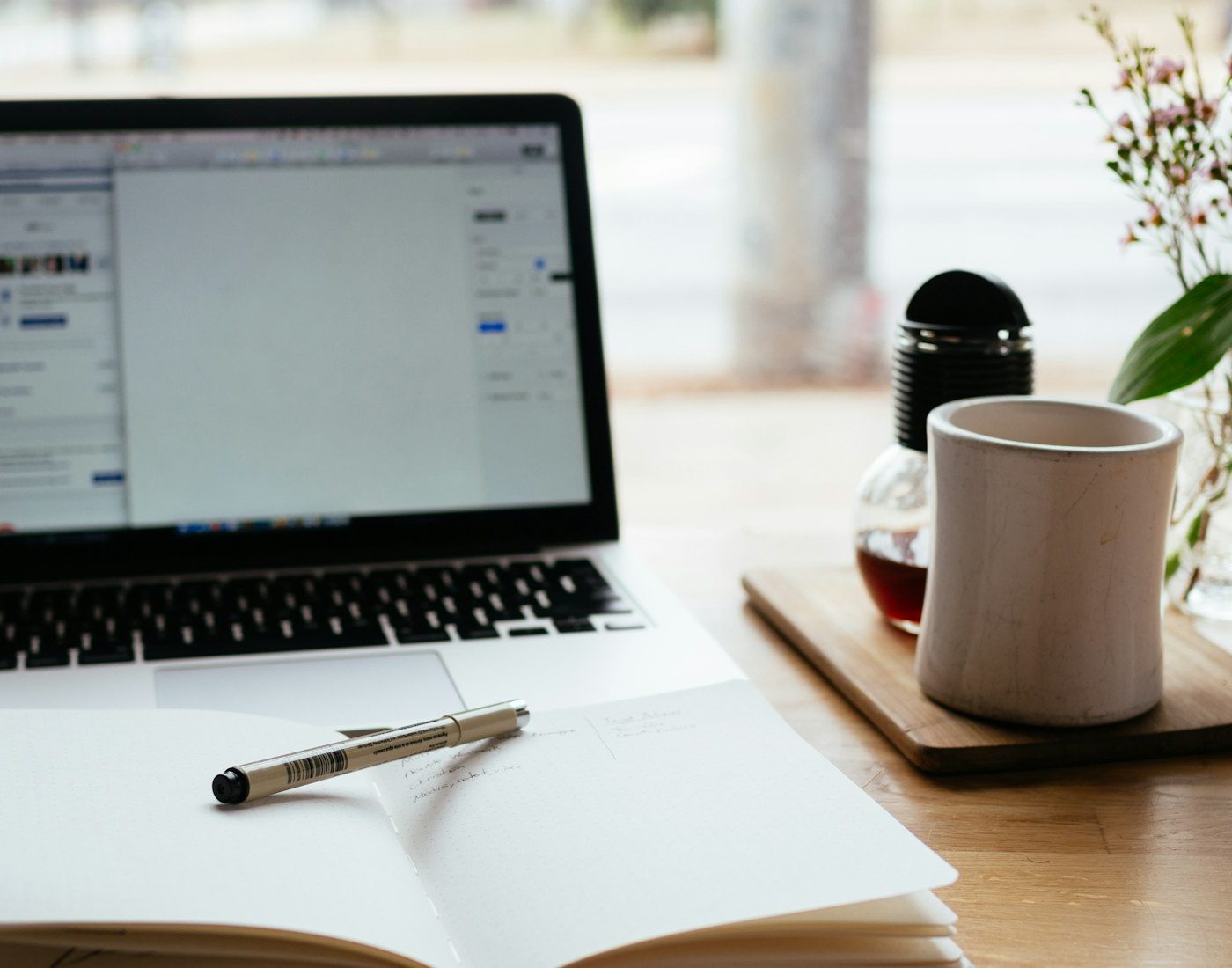 Open notebook and pen beside a laptop and coffee