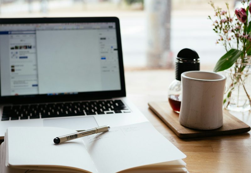 Open notebook and pen beside a laptop and coffee